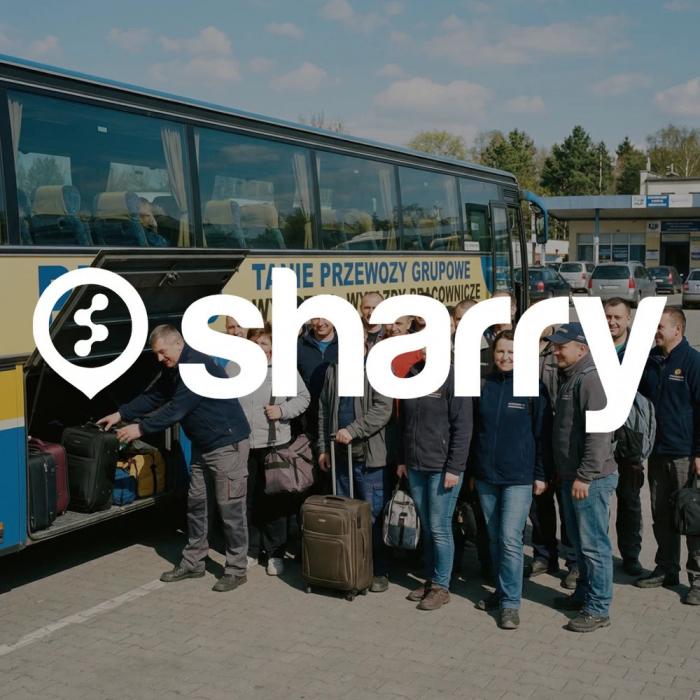  Sharry na tle grupy ludzi stoj�cych przy autobusie, podczas gdy kierowca �aduje walizki do baga�nika 